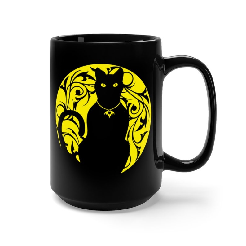 May include: Black ceramic mug featuring a yellow silhouette of a cat sitting in a moon with floral designs.