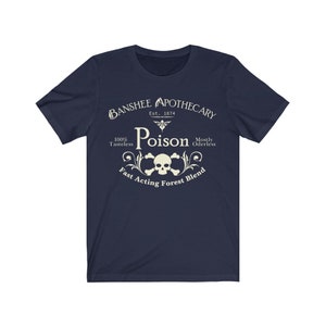 Puede incluir: Una camiseta azul marino con un dise&ntilde;o gr&aacute;fico blanco de una calavera y huesos cruzados con el texto "Banshee Apothecary Est. 1874 Poison 100% Tasteless Mostly Oderless Fast Acting Forest Blend".