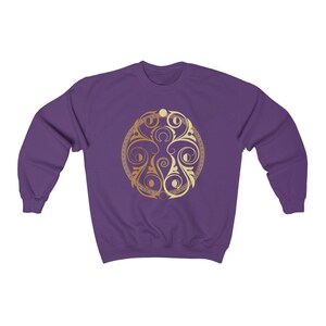 May include: Purple sweatshirt with a gold and cream colored circular design featuring a stylized floral pattern.