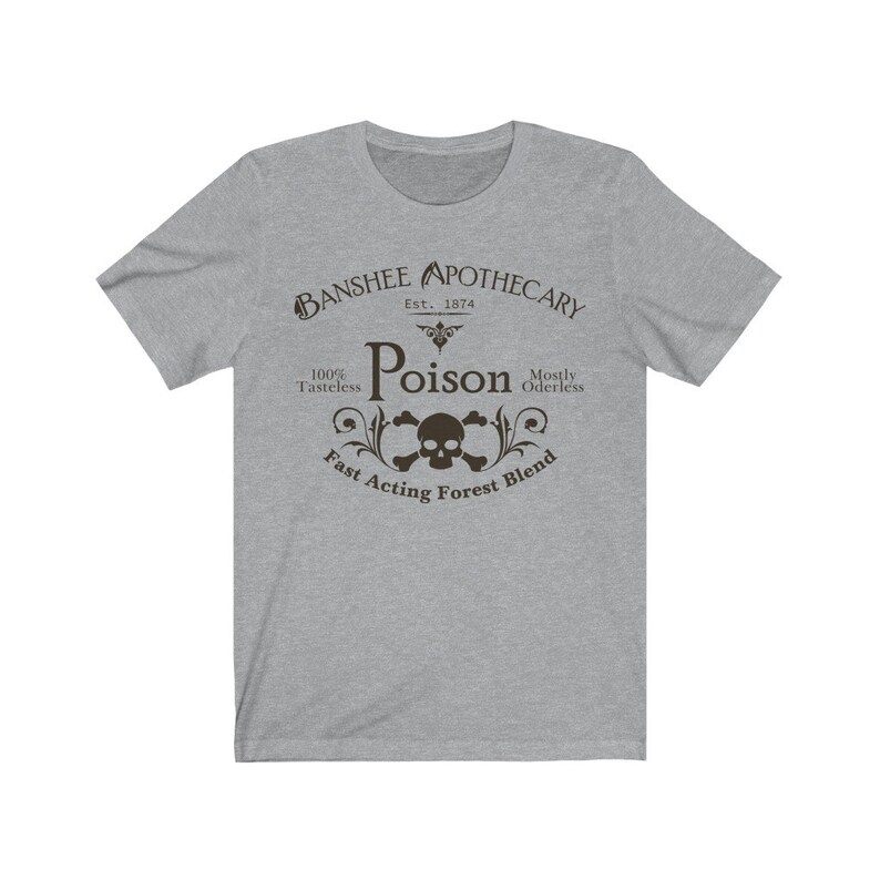 Puede incluir: Una camiseta gris con un dise&ntilde;o gr&aacute;fico negro que dice "Banshee Apothecary Est. 1874 Poison 100% Tasteless Mostly Oderless Fast Acting Forest Blend". El gr&aacute;fico tambi&eacute;n incluye una calavera y huesos cruzados.