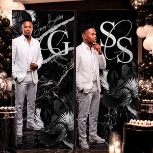 May include: A large black and white birthday backdrop featuring a marble pattern, tropical leaves, and large silver letters G and SS. The text Happy Birthday is printed in script. The backdrop is flanked by black, white, and silver balloons.