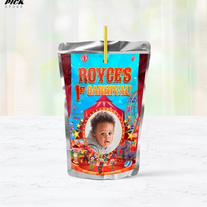 Puede incluir: Una bolsa de jugo plateada con una etiqueta colorida con temática de carnaval. La etiqueta presenta una foto de un niño pequeño, el texto "Royce's 1st Carnival!" y una carpa a rayas rojas y blancas.