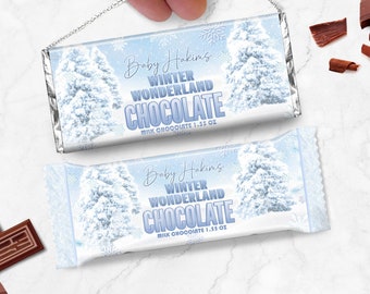 May include: A blue and white chocolate bar wrapper with a winter wonderland theme. The wrapper features a snowy forest scene with trees and snowflakes. The text on the wrapper reads "Baby Hakim's Winter Wonderland Chocolate Milk Chocolate 1.55 oz".