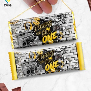 以下が含まれることがあります： グラフィティのデザインが施された、金色と黒色のチョコレートバーの包装紙。包装紙には、ブームボックス、王冠、そして「Jaremy the Big One」という文字が書かれています。