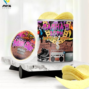 以下が含まれることがあります： 落書き風のデザインが施されたカスタムラベルのポテトチップスの缶。ラベルには「Sasha's 25th Birthday Bash!」と金色のチェーンとドルマークが書かれている。缶は、大理石の表面に置かれ、隣にはポテトチップスの山が置かれている。