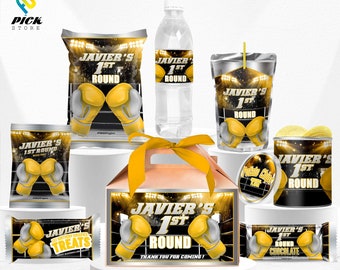 Könnte beinhalten: Ein Box-Party-Geschenkset mit verschiedenen Artikeln, darunter eine Geschenkbox, eine Tüte Chips, eine Saftbox, eine Wasserflasche, ein Schokoriegel und eine Dose Kartoffelchips. Die Artikel sind mit einem schwarzen und goldenen Boxring-Design und dem Text "Javier's 1st Round" verziert.