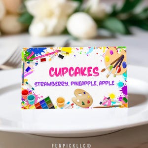 May include: A colorful printable sign with paint splatters and art supplies, reading "CUPCAKES" and "STRAWBERRY, PINEAPPLE, APPLE".