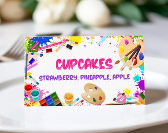 May include: A colorful printable sign with paint splatters and art supplies, reading "CUPCAKES" and "STRAWBERRY, PINEAPPLE, APPLE".