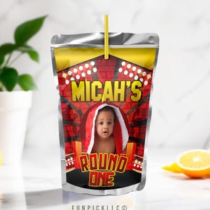 May include: A silver juice pouch with a red and yellow boxing ring design. The pouch has a photo of a baby in a red robe and the text "Micah's Round One".