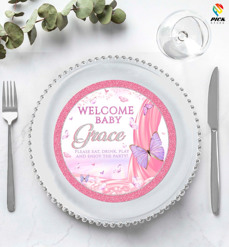 May include: White plate with a pink and white round paper plate with a pink glitter border. The paper plate has a pink and white butterfly design with the text "Welcome Baby Grace" and "Please eat, drink, play and enjoy the party!"