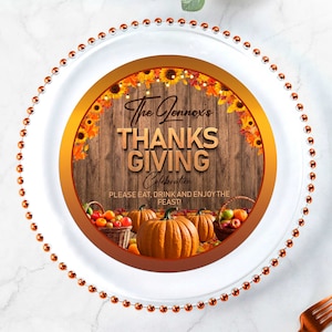 Puede incluir: Un plato blanco con borde de cuentas, con un diseño temático de Acción de Gracias. El diseño incluye calabazas, cestas de frutas y el texto "The Lennox's THANKSGIVING Celebration". El plato está decorado con girasoles y hojas de otoño.