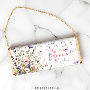 May include: A white clutch purse with a gold chain strap. The purse has a floral design with butterflies and the text "Baby in Bloom Mikayla's Baby Shower".