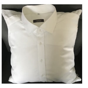 May include: White pillow with a white dress shirt on top of it. The shirt has a collar, buttons, and a label that says "i Tailor".