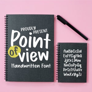Könnte beinhalten: Zwei schwarze Spiralblöcke auf rosa Untergrund. Der größere Block hat den Text "Proudly Present Point of View Handwritten Font" auf der Vorderseite. Der kleinere Block zeigt das Alphabet in einer handschriftlichen Schrift.