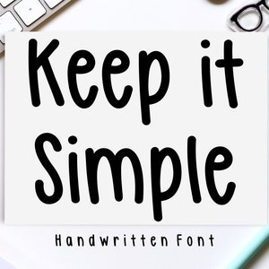 May include: A white card with black text that reads "Keep it Simple" in a handwritten font. The text "Handwritten Font" is also written in black below the main text.