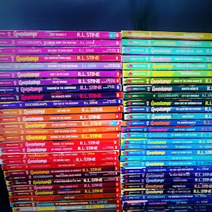 Pode incluir: Uma pilha de livros Goosebumps de R.L. Stine. Os livros est&atilde;o dispostos em duas colunas, com as lombadas voltadas para fora. Os livros s&atilde;o de cores diferentes, com t&iacute;tulos como "Deep Trouble", "Welcome to Dead House" e "Say Cheese and Die".