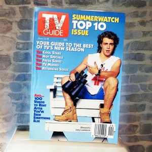 May include: A magazine cover featuring a young man sitting on a bench holding binoculars. The magazine is titled "TV Guide" and the cover story is "Summerwatch Top 10 Issue".