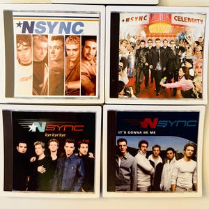 May include: Five *NSYNC CD covers are displayed. The covers showcase images of the band and album titles including "No Strings Attached", "Celebrity", "Bye Bye Bye", and "It's Gonna Be Me". The covers are presented in white frames.