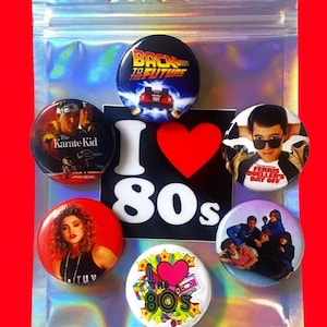 May include: A set of six 80s themed button pins in a clear plastic bag. The pins feature images from popular 80s movies and music, including Back to the Future, The Karate Kid, Ferris Bueller's Day Off, and Madonna. The pins are all round and have a white background with colorful images.
