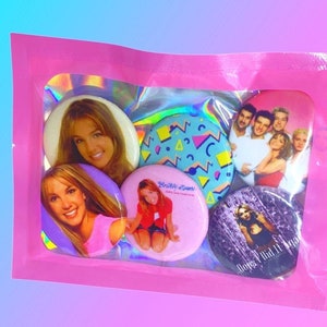 May include: A pink plastic bag with a clear window containing six round buttons. The buttons feature images of popular 90s pop stars, including Britney Spears and the Backstreet Boys. The buttons are a fun and nostalgic way to show your love for 90s pop culture.