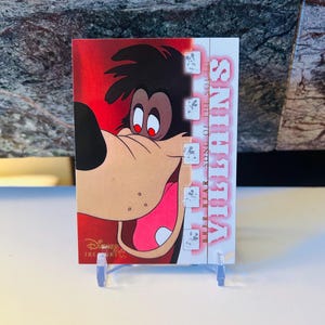 May include: A Disney Treasures trading card featuring Brer Bear from "Song of the South." The card has a red background with the character's face prominently displayed. The card is on a clear plastic stand.