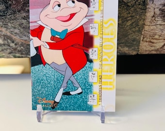 Puede incluir: Una tarjeta coleccionable de Disney con Thaddeus Toad de "Las Aventuras de Ichabod y Mr. Toad". La tarjeta muestra una rana de dibujos animados con abrigo rojo y pajarita azul. La tarjeta se muestra en un soporte de plástico transparente.