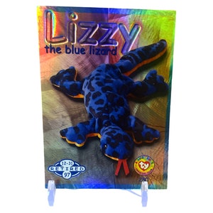 Puede incluir: Un juguete de peluche de lagarto azul y negro con vientre amarillo y lengua roja. El juguete está etiquetado como "Lizzy the blue lizard" y "Retired 12-31-97".