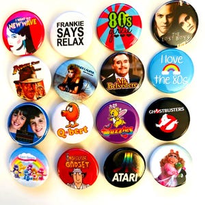 Könnte beinhalten: Eine Sammlung bunter runder Ansteckbuttons mit Popkultur-Referenzen. Designs beinhalten Texte wie "Frankie Says Relax", "80s girlie" und Bilder aus "The Lost Boys", "Ghostbusters" und "Inspector Gadget".
