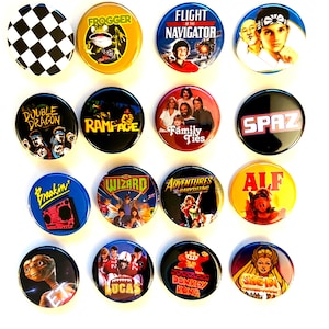 May include: A collection of sixteen round pinback buttons with various designs. The buttons feature images and text from movies, TV shows, and video games, including "Flight of the Navigator," "Family Ties," and "Donkey Kong." The buttons are in various colors, including black, blue, yellow, and red.