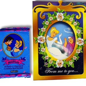 May include: A Cinderella card game set with 14 cards, 1 pop-out, and 1 activity card per pack. The card game set is packaged in a blue box with a picture of Cinderella and Prince Charming. The box is next to a gold card with a picture of Cinderella and the text "From me to you..."