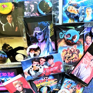 Puede incluir: Una colección de recuerdos de música y cine de los años 80 y 90, incluyendo botones, tarjetas coleccionables y pósters. Los artículos presentan imágenes de Madonna, Ferris Bueller, Los Goonies, Regreso al futuro, y más.