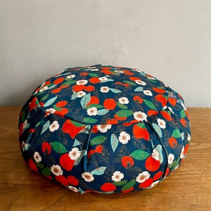 Peut inclure: Un coussin de méditation rond en tissu bleu foncé avec un motif répétitif de fruits orange, de fleurs blanches et de feuilles vertes.
