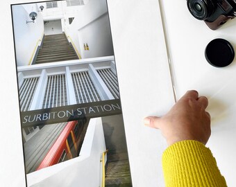 May include: A black and white photo of a train station with the text "SURBITON STATION" printed on the image. The photo is divided into three sections, showing a staircase, a white wall with a series of vertical bars, and a red train car.