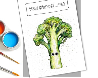 May include: A greeting card with a hand-drawn illustration of a broccoli with googly eyes. The card says "You Brocc! ...Oli" in black text.