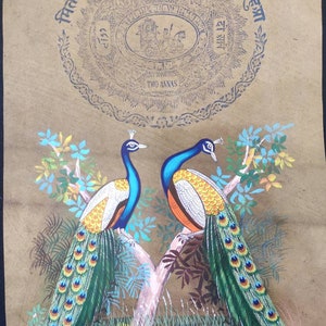 May include: An antique painting featuring two peacocks perched on a tree branch. The birds have blue heads, white and orange bodies, and vibrant green and blue tail feathers. The artwork includes text and a circular emblem at the top.