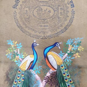 May include: A vintage painting featuring two peacocks perched on a tree branch. The birds have blue, green, and orange plumage. The background is a tan color with blue text and a circular design that reads "TWO ANNAS".