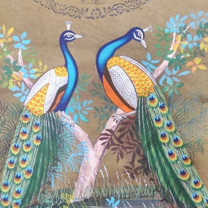 May include: A detailed painting of two peacocks perched on a tree branch. The birds have blue necks, white and orange chests, and vibrant green and yellow tail feathers. The background is a warm brown with floral accents and the text "TWO ANNAS".