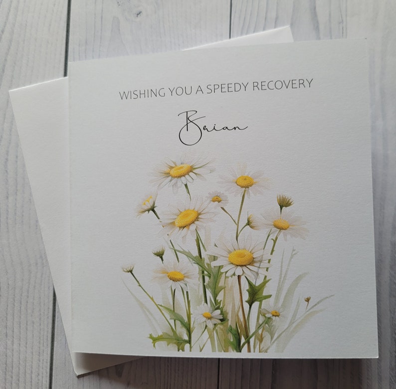 May include: A white card with a watercolour illustration of white daisies with yellow centres. The card says "Wishing you a speedy recovery Brian".