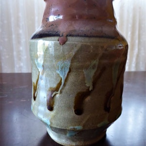 May include: A brown and gray ceramic vase with a mottled glaze. The vase has a rounded body and a wide mouth.