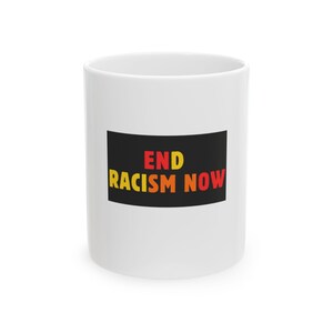 May include: A white ceramic mug featuring a rectangular black graphic on the front. The text END RACISM NOW is printed in bold, multi-colored letters, with END in red and yellow, and RACISM NOW in yellow, orange, and red gradient tones.