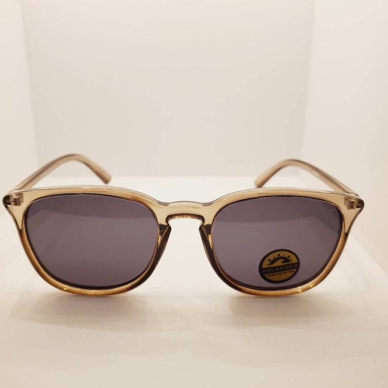 May include: A pair of brown, square-shaped sunglasses with polarized lenses. The sunglasses have a gold-colored logo on the right lens that says "POLARIZED".