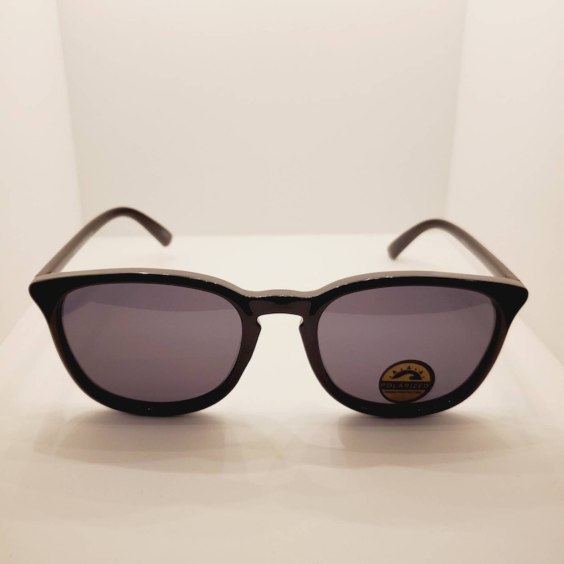 May include: Black sunglasses with polarized lenses. The lenses are dark grey and the frame is black.