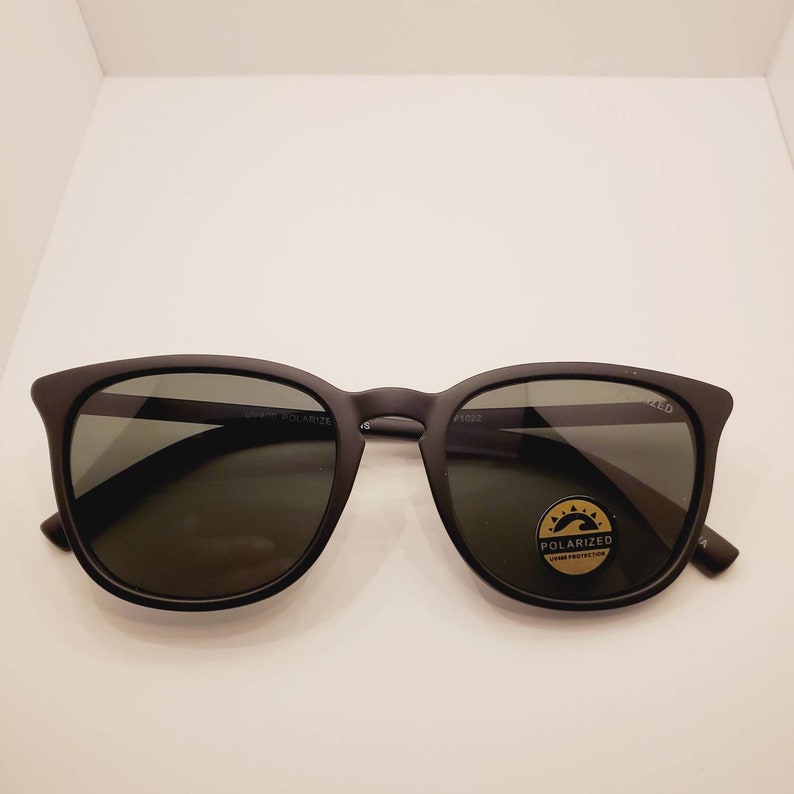 May include: Black sunglasses with polarized lenses. The sunglasses have a black frame and a gold label that says "Polarized UV400 Protection".