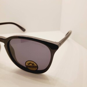 May include: Black sunglasses with polarized lenses. The lenses are tinted a dark grey color. The sunglasses have a black frame and the words "POLARIZED" are printed on the right lens.