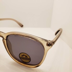 May include: A pair of brown polarized sunglasses with a clear frame. The sunglasses have a dark grey lens and a small sticker on the lens that says "Polarized UV Protection".