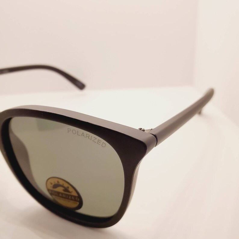 May include: Black sunglasses with polarized lenses. The sunglasses have a black frame and a silver label that says "POLARIZED".