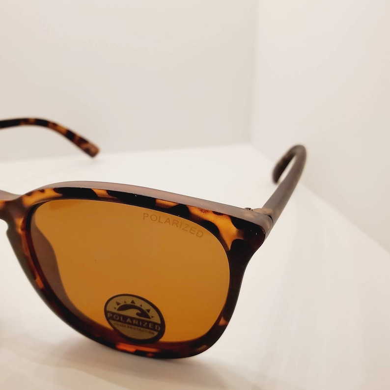 May include: Tortoise shell sunglasses with brown lenses. The sunglasses have the word "POLARIZED" printed on the frame and a small circular label that says "POLARIZED" with a wave design.