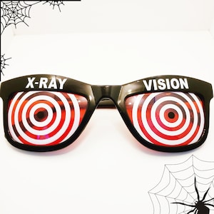 Puede incluir: Gafas de plástico negro de novedad con patrones de diana rojos y blancos. La lente izquierda dice "X-RAY" y la lente derecha dice "VISION".