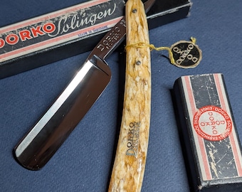 May include: A straight razor with a bone handle. The razor is made by the company "DORKO Solingen" and is made in Germany. The razor is in its original box.