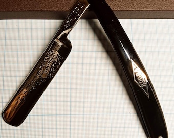 May include: A vintage straight razor with a black handle and a silver blade. The blade is engraved with the words "Solingen" and "R.U.C.K.A."